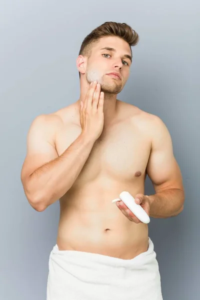 Young caucasian man using facial moisturizer — Stock Photo, Image