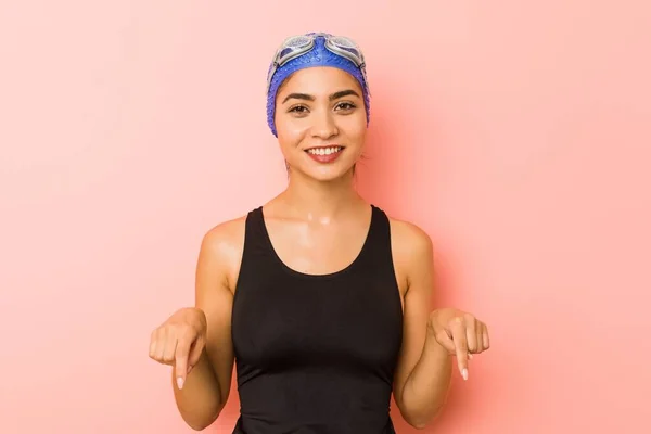 Young arab swimmer woman isolated points down with fingers, positive feeling.