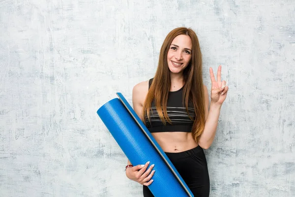 年轻的高加索女运动员拿着一个用手指展示二号的垫子 — 图库照片