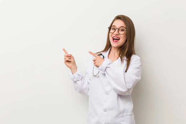 年轻的女医生靠着一面白色的墙兴奋地拿着一个复制品放在手掌上 — 图库照片