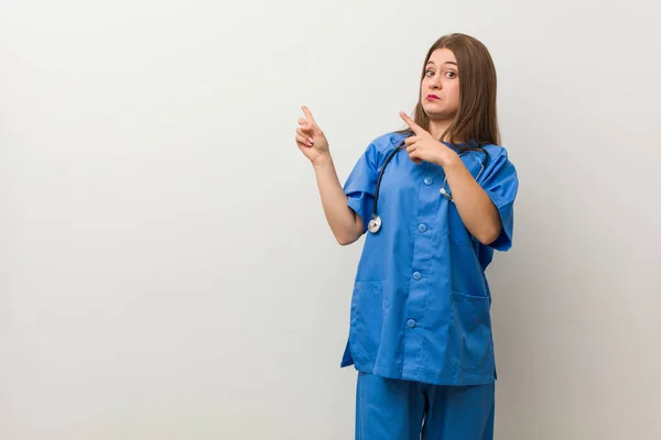 Νεαρή Νοσοκόμα Γυναίκα Ένα Λευκό Τοίχο Σοκαρισμένη Δείχνοντας Δείκτες Δάχτυλα — Φωτογραφία Αρχείου