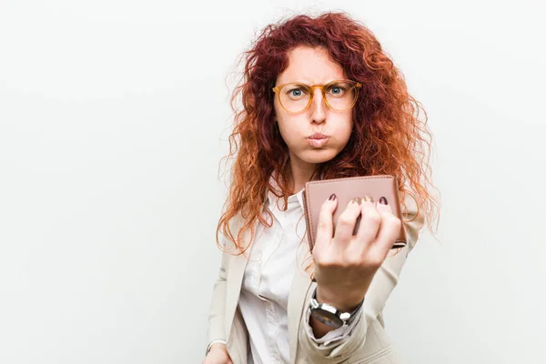 Young caucasian redhead woman holding a wallet showing fist to camera, aggressive facial expression.