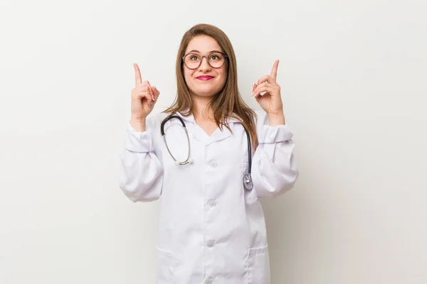 Jonge Doktersvrouw Tegen Een Witte Muur Geeft Met Beide Voorvingers — Stockfoto