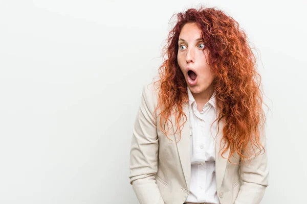 Young natural redhead business woman isolated against white background being shocked because of something she has seen.