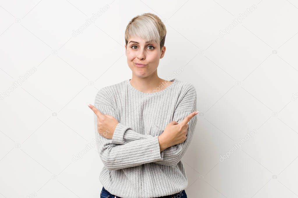 Young curvy caucasian woman isolated on white background points sideways, is trying to choose between two options.