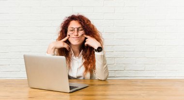 Genç, kızıl saçlı, laptopuyla çalışan kıvırcık kadın iki seçenek arasında şüphe duyuyor..