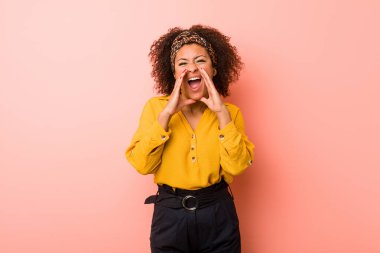 Genç Afrikalı Amerikalı kadın pembe arka planda heyecanlı bir şekilde bağırıyor.