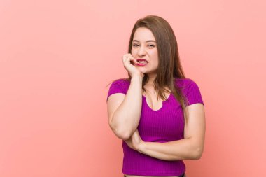 Genç İspanyol kadın pembe bir duvara yaslanmış tırnak yiyor, gergin ve çok endişeli..