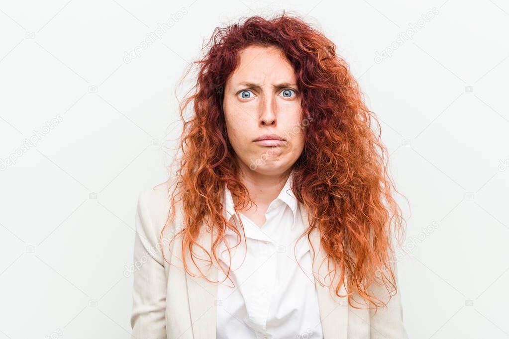 Young natural redhead business woman isolated against white background shrugs shoulders and open eyes confused.