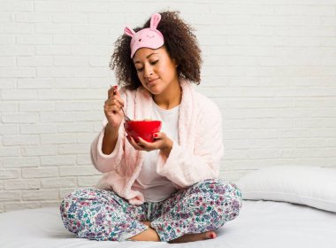 Genç afrikalı amerikalı kadın yatakta bir tahıl kase yemek