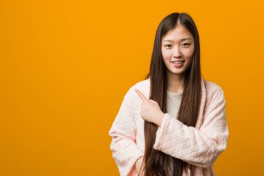 Pijamalı genç Çinli kadın gülümsüyor ve boş alanda bir şeyler gösteriyor..