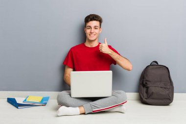 Evinin zemininde dizüstü bilgisayar tutan genç bir öğrenci.