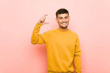 Genç İspanyol adam ön parmakları ile küçük bir şey tutan, gülümseyen ve kendinden emin.