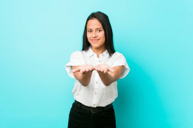 Mavi bir duvara yaslanmış, elinde avuç içi bir şeyle kameraya sunan İspanyol asıllı havalı bir kadın..