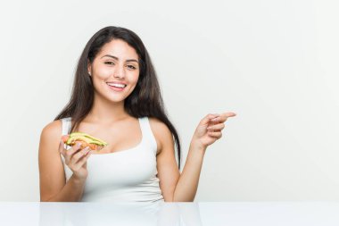 Avokado tostu tutan genç İspanyol kadın işaret parmağıyla işaret ederek gülümsüyor..