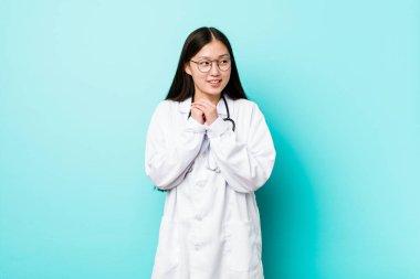 Genç Çinli doktor ellerini çenesinin altında tutuyor ve mutlu bir şekilde yan tarafa bakıyor..