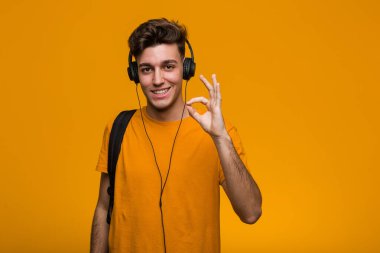 Kulaklıkla müzik dinleyen genç, havalı bir öğrenci kendini işaret ederek, geniş bir gülümsemeyle şaşırdı..