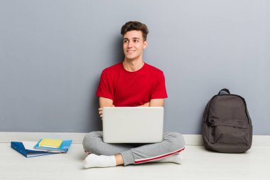 Evinin zemininde dizüstü bilgisayar tutan genç bir öğrenci.