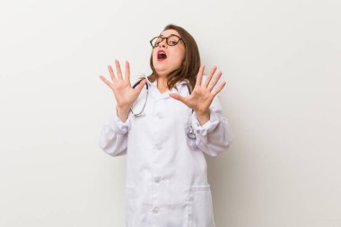 Beyaz bir duvara dayanmış genç bir doktor kadın, yakın bir tehlike nedeniyle şoka uğruyor.