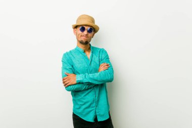 Yaz kıyafetleri giyen, hoşnutsuzca kaşlarını çatan, kollarını kavuşturan genç bir İspanyol..