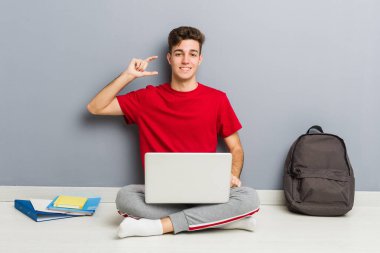 Evinin zemininde dizüstü bilgisayar tutan genç bir öğrenci.