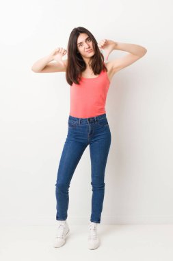 Beyaz arka planda genç bir kadın baş parmağını aşağı gösteriyor ve hoşlanmadığını ifade ediyor..