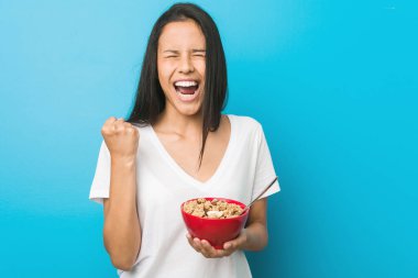 Genç İspanyol bir kadın elinde mısır gevreği kasesiyle gamsız ve heyecanlı bir şekilde tezahürat yapıyor. Zafer konsepti.