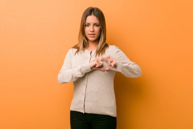 Genç otantik karizmatik gerçek insanlar kadın bir duvara karşı gülümseyen ve elleriyle bir kalp şekli gösteren.