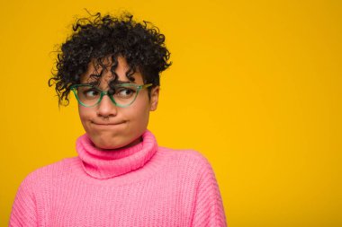 Pembe kazak giyen Afro-Amerikalı genç bir kadın kafası karışmış, kararsız ve kendinden emin değil..
