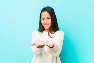 Genç, güzel, İspanyol bir kadın avuçlarıyla bir şey tutuyor ve kameraya teklif ediyor..