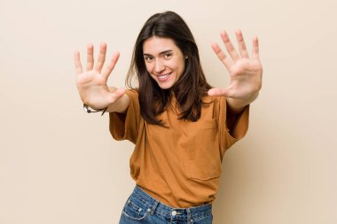 Genç esmer kadın bej arka planda 10 numarayı elleriyle gösteriyor..