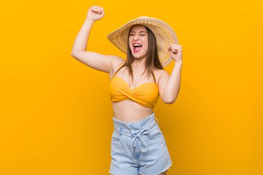 Hasır şapkalı genç beyaz kadın, yaz mevsiminde özel bir günü kutluyor, zıplıyor ve enerjiyle kollarını kaldırıyor..