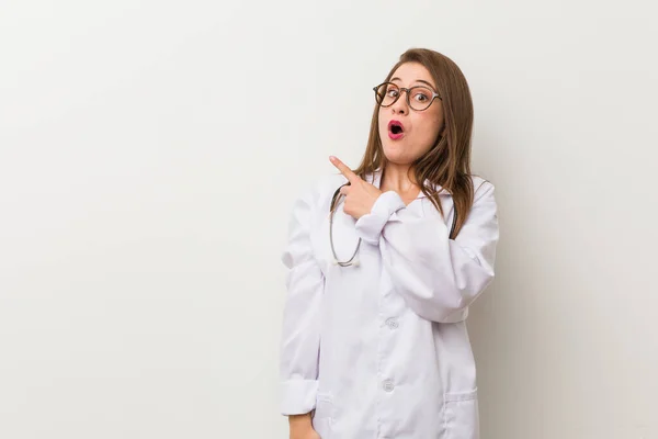 Jonge Dokter Vrouw Tegen Een Witte Muur Wijst Naar Zijkant — Stockfoto