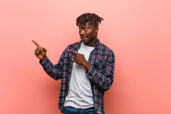 Young african black man shocked pointing with index fingers to a copy space.