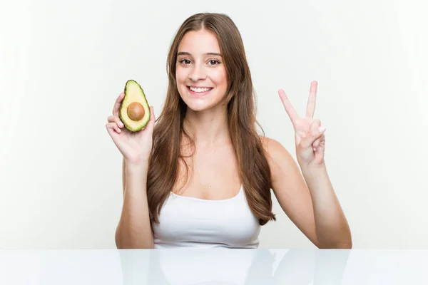 Young Caucasian Woman Holding Avocado Showing Number Two Fingers — Stock Photo, Image