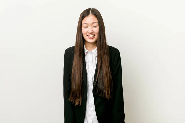 Young pretty chinese business woman laughs and closes eyes, feels relaxed and happy.