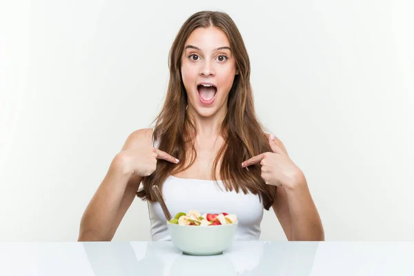 Giovane Donna Caucasica Mangiare Frutta Ciotola Sorpreso Indicando Stesso Sorridendo — Foto Stock