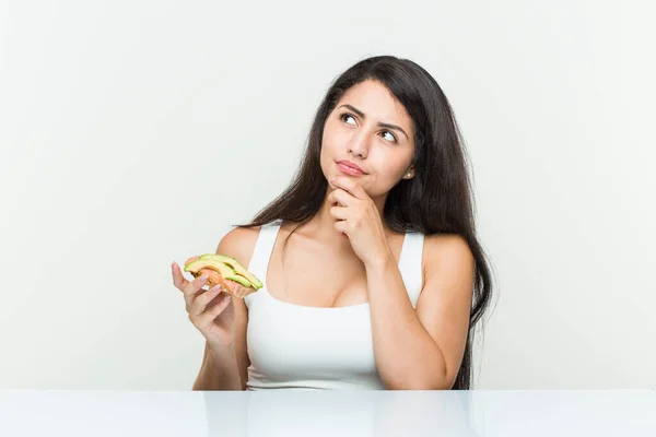 Jonge Spaanse Vrouw Houdt Een Avocado Toast Kijken Zijwaarts Met — Stockfoto
