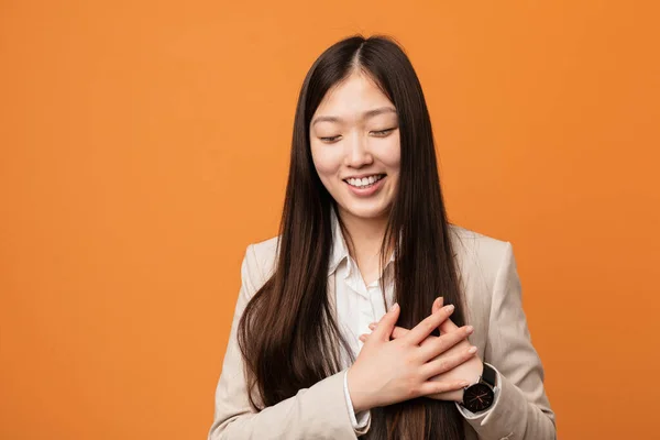 Young business chinese woman laughing keeping hands on heart, concept of happiness.