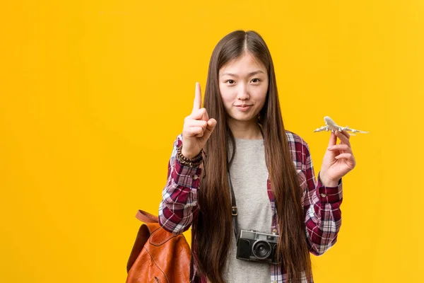 拿着飞机图标的年轻亚洲女人用手指展示了头号人物 — 图库照片