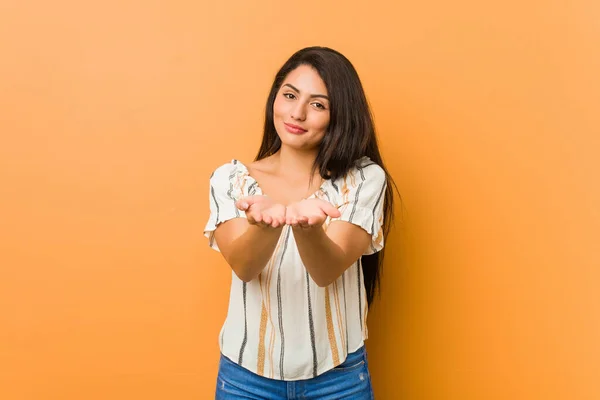 Young curvy woman holding something with palms, offering to camera.