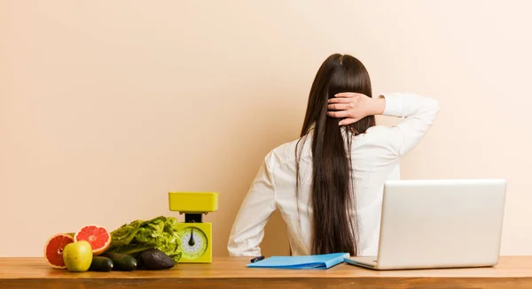 Young nutritionist chinese woman working with her laptop from behind thinking about something.