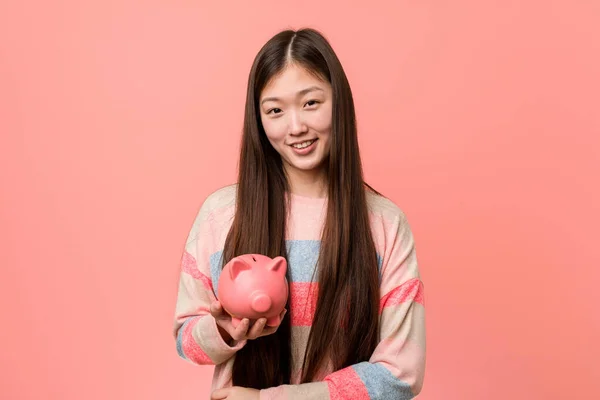 年轻的亚洲女人抱着小猪银行微笑着 自信地交叉着双臂 — 图库照片