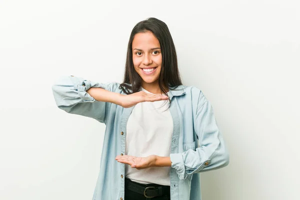 Young hispanic woman holding something with both hands, product presentation.