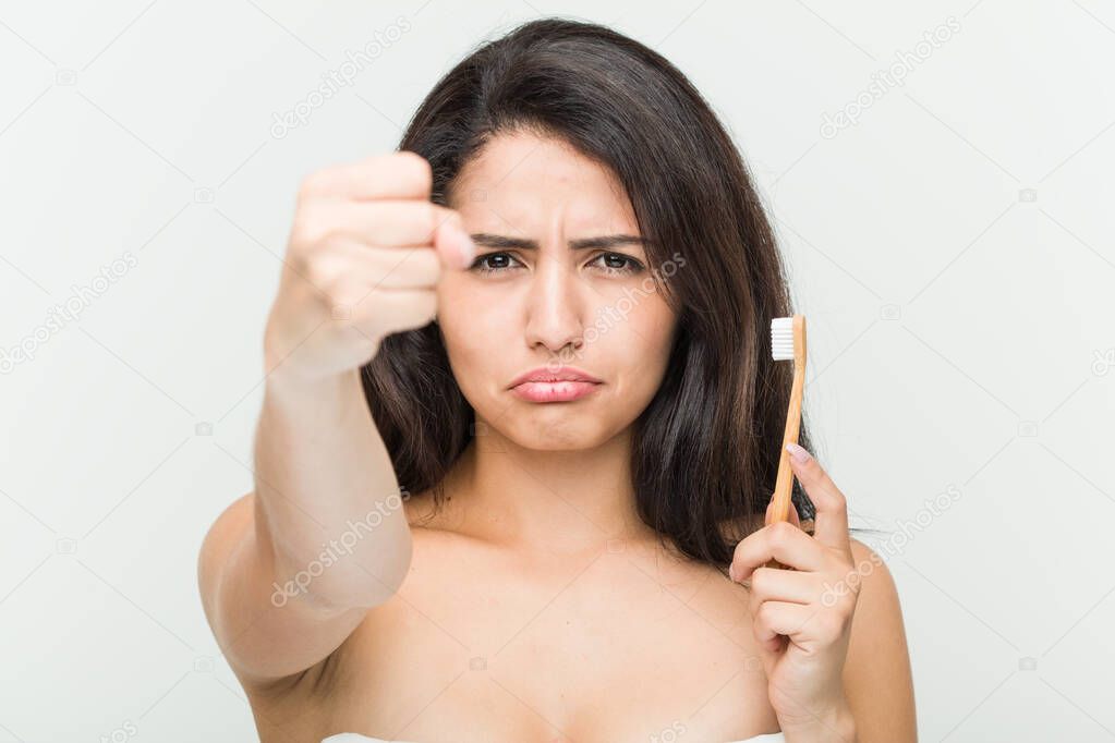 Young hispanic woman holding a toothbrush showing fist to camera, aggressive facial expression.