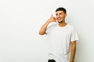 Genç İspanyol adam parmakları ile bir cep telefonu arama jesti gösteren.