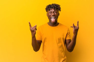 Sarı arka planda rastalar takan genç siyah adam parmaklarıyla taş hareketi gösteriyor.