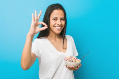 Genç İspanyol kadın elinde mısır gevreği kasesiyle neşeli ve kendinden emin bir şekilde iyi bir jest yapıyor..