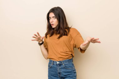 Genç esmer kadın, bej bir arkaplanda yakın bir tehlike nedeniyle şoka uğruyor.