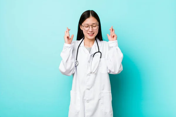 Young chinese doctor woman crossing fingers for having luck